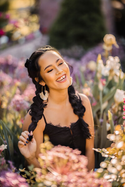 woman with long dark braids sitting in a field of purple flowers laughing
