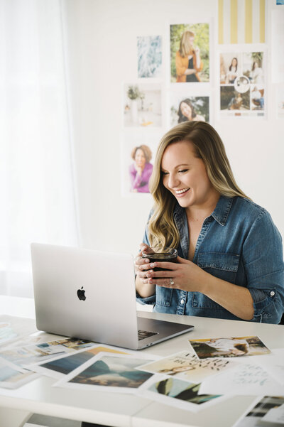 Krista Marie, a brand photographer and website designer, sitting at a desk with a cup of coffee and speaking into her laptop