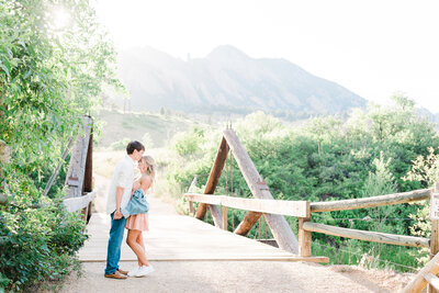 outdoor engagement pictures with man and woman holding hands on a bridge with mountains in the distance taken by denver wedding photographer