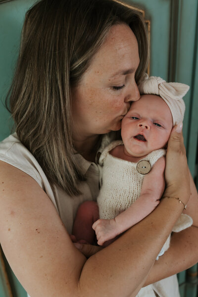 Mama houdt pasgeboren baby vast in haar armen tijdens newbornshoot