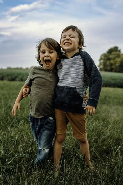 Two boys stand together outside in the grass and smile at the camera