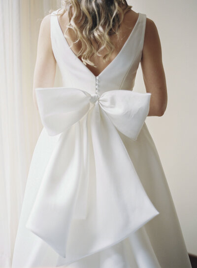 A close up of the back of a bridal gown with a large white bow. 