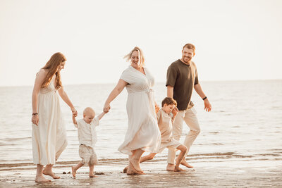 Familie van 5 lopend op het strand hand in hand