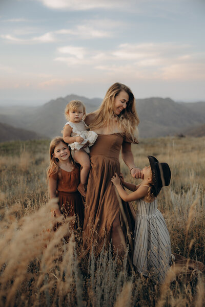 A mom in a flowing dress cuddling with her three daughters in Rist Canyon by Grey Rock