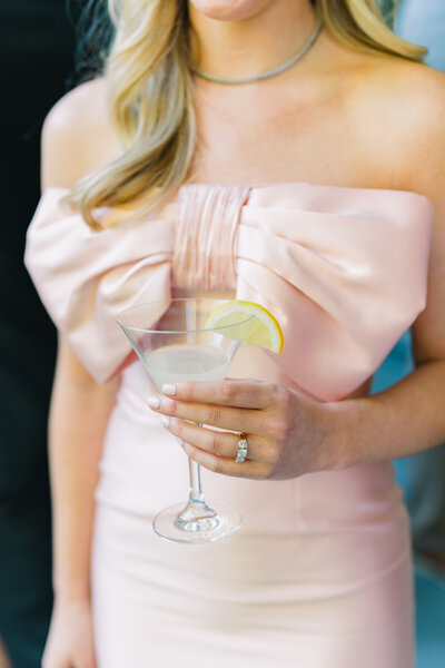 Pink bow maid of honor dress holding a martini with a lemon garnish at cocktail hour during charleston spring wedding.