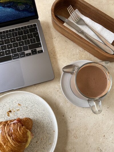 A laptop, croissant, and coffee served on a table.