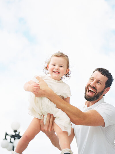 Brunette dad flies toddler daugher through the air as she smiles