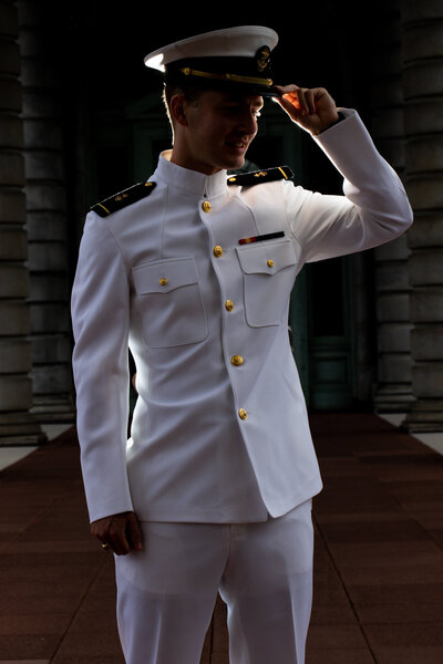 Backlit Navy Officer in white uniform holding hat.