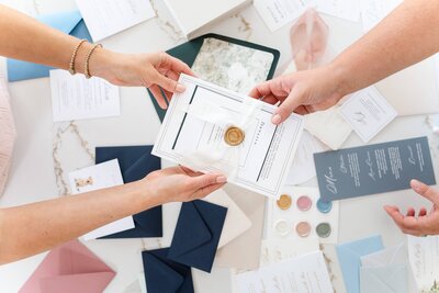 Wedding stationers holding custom five-piece invitation suite tied together with a silk ribbon and gold wax seal