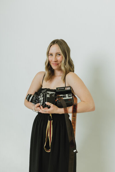 woman wearing a black hat and dress holding a camera while gently smiling