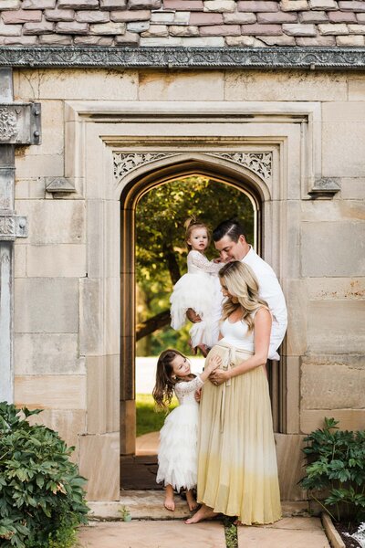 A family with two young children standing in front of an ornate stone doorway, sharing a moment together during their maternity photography session.