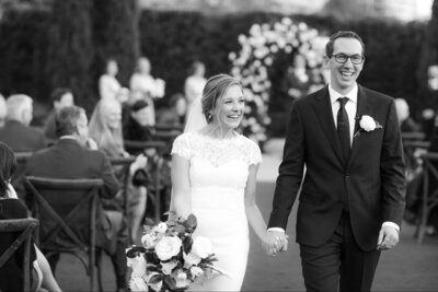 Black and white photo of bride and groom holding hands walking back down the aisle