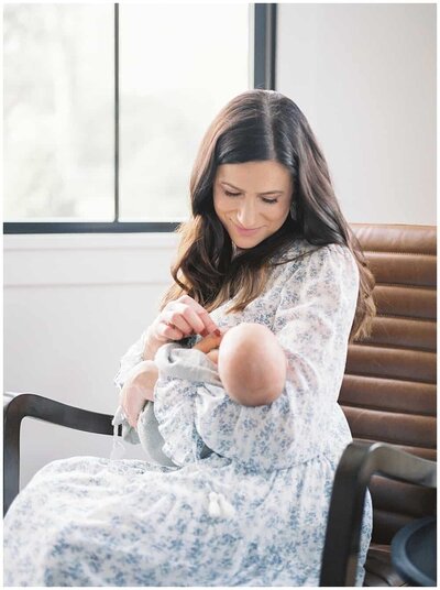 A mother holds her newborn baby and touches his fingers and smiles down at him during their newborn photography session in Northern VA by DC Newborn Photographer Marie Elizabeth Photography