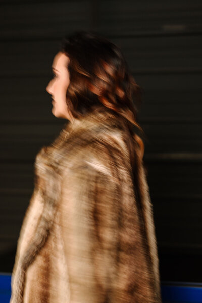 Blurry artistic side portrait of Juliet Trnka in a fur coat with a dark background