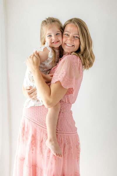A mom wearing a pink dress holding her first born daughter during her maternity photoshoot in Studio in Savannah, Ga