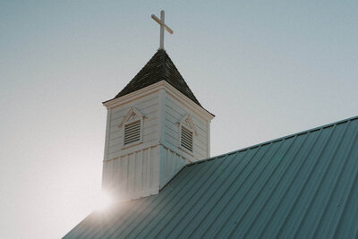 White chapel with cross at peak and sun beaming behind