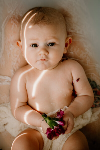 Close up photo of baby girl holding flower laying down in milk bath.