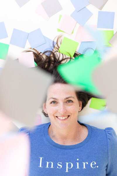 social media strategist and course creator is lying on the white floor with sticky notes in different colors such as blue, green, gray and light pink
