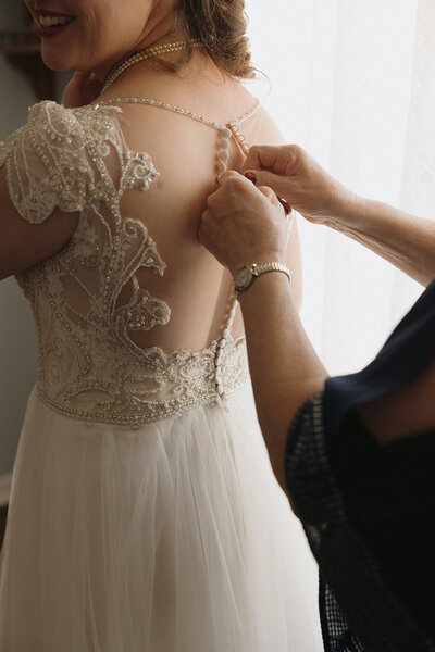 Mom zipping up daughters wedding dress 
