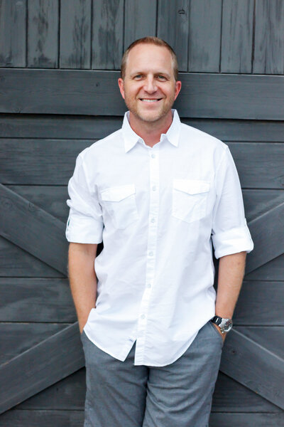 A man in a white shirt posing for his headshot images in front of a gray door.