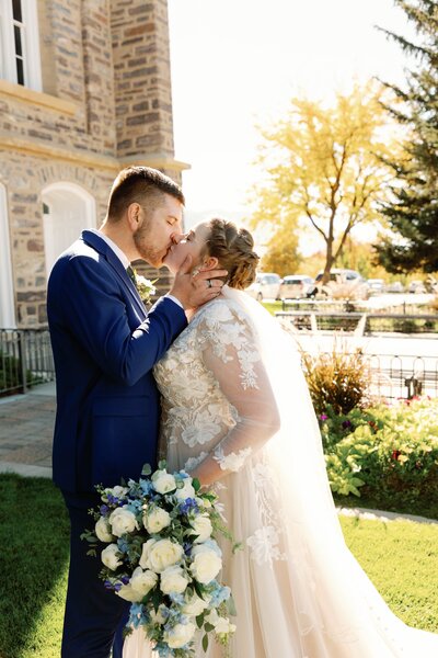 bride and groom kissing outside the Logan LDS Temple bride holding white and blue wedding bouquet