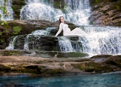 Breathtaking maternity portrait of an expectant mother in a white lace gown by a cascading waterfall, captured in Gardner, Kansas. Ideal for adventurous families seeking unique and natural maternity photography in the Kansas City area.