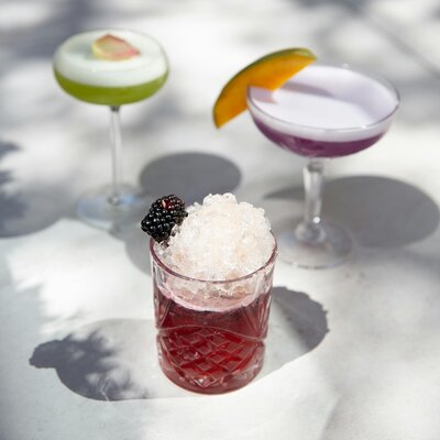 three craft cocktails. two in coupe glasses as martinis. one bramble in a rocks glass.