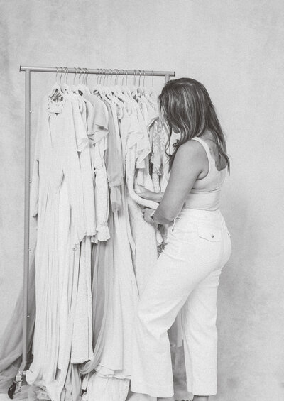 Portrait photographer browsing a collection of light-toned dresses, showcasing a full-service wardrobe experience in studio.
