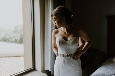 A bride looking out the window of her dimly lit bridal suite.