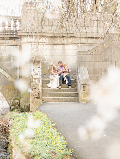 Beautiful portrait of a family sitting on stone steps through the blooming petals of a tree
