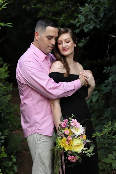 Married couple with flowers standing and hugging near dark trees