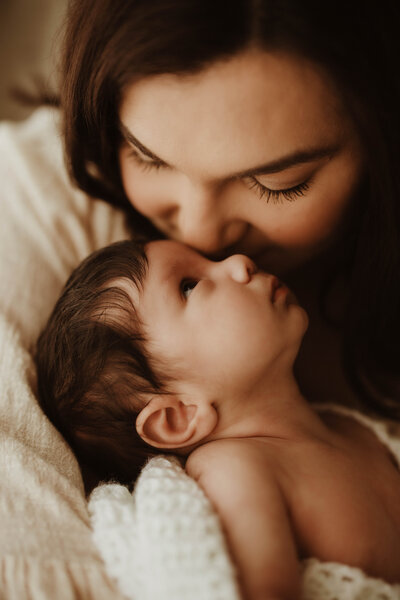 Mother kissing newborn baby’s forehead in soft natural light, Sydney newborn photography.