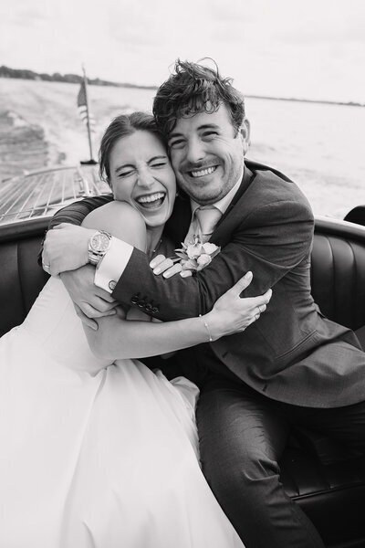 black and white photograph of bride and groom happily embracing after their wedding riding a boat in minnesota image by tom thornton photography