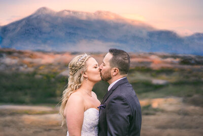 Stunning photograph capturing a bride and groom sharing a heartfelt kiss amidst a mountainous backdrop, epitomizing the grandeur and romance of their special day.
