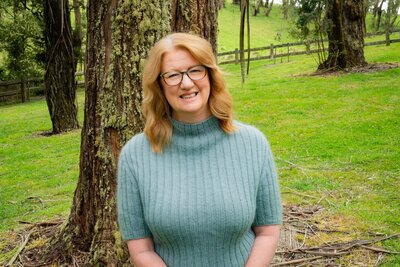 Suzanne Harrison wearing a blue turtleneck sweater in front of a tree 