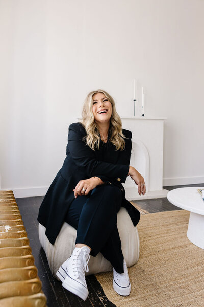 Calgary Realtor Leigh Kormos laughing while sitting on an off-white chair