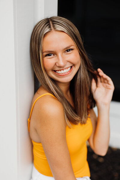 Close up portrait of senior girl in orange top twirling her hair