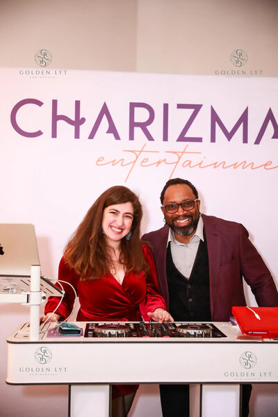 Charizma Entertainment team members Nicole and Marz smiling behind a DJ booth at a Chicago event