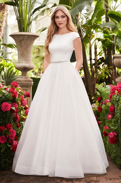 Crêpe and Organza Wedding Dress. Crêpe bodice with boat neckline and cap sleeves. Crêpe belt with beaded appliqué at waist. Full Organza skirt with pockets and 4” horsehair on hem.