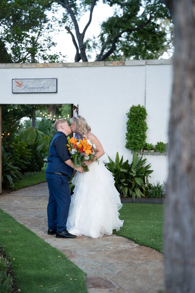 An Austin-based wedding photographer captures a beautiful moment as the bride and groom share a tender kiss in front of a white building.