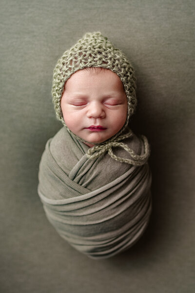 Overhead portrait of newborn boy with bonnet and swaddled in green wrap in Jacksonville, FL.
