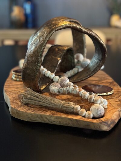 Organic wood tray with sculptural metallic centerpiece and decorative beads styled on a dining table in Phoenix, AZ.