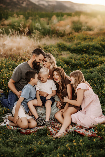 Family Photographer,  large family snuggled on a blanket in the yellow flowers and spring grass