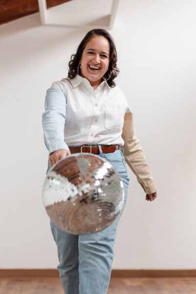 woman smiling while walking forward and swinging a disco ball with one hand