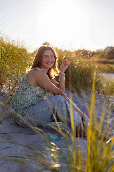 Image of graduating high school sitting on the beach in tall grass, while smiling at the camera.