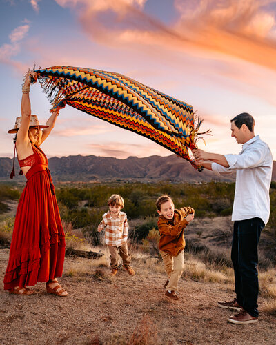 family playing in the desert with a blanket and cotton candy sunset