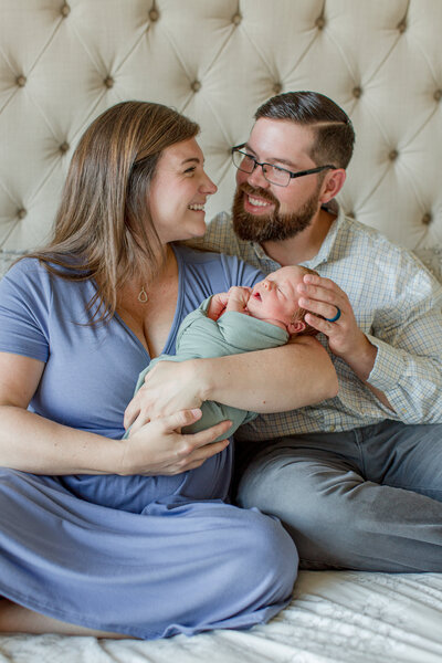 Family photo in Boone, NC of a mother and father smiling at each other while holding their infant son during a newborn family session.