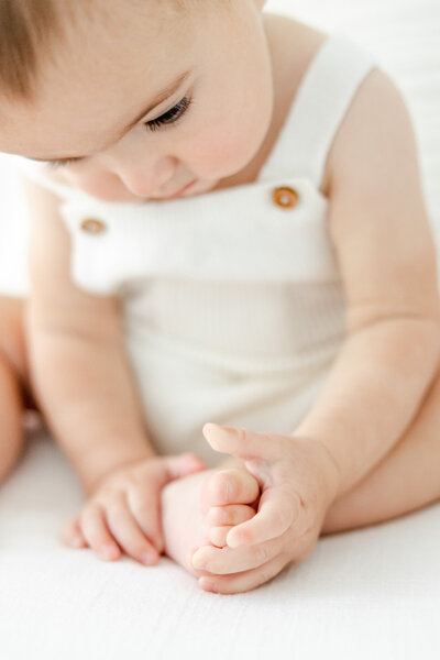 6 month old baby boy sits and plays with his toes during milestone portrait session