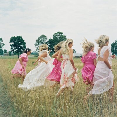 Bride with bridesmaids walking through field by wedding film photographer Noble Photo Co
