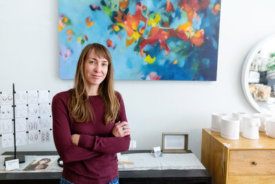 Artist Shantael Sleight standing confidently in her studio, arms crossed, with a vibrant abstract painting displayed behind her.